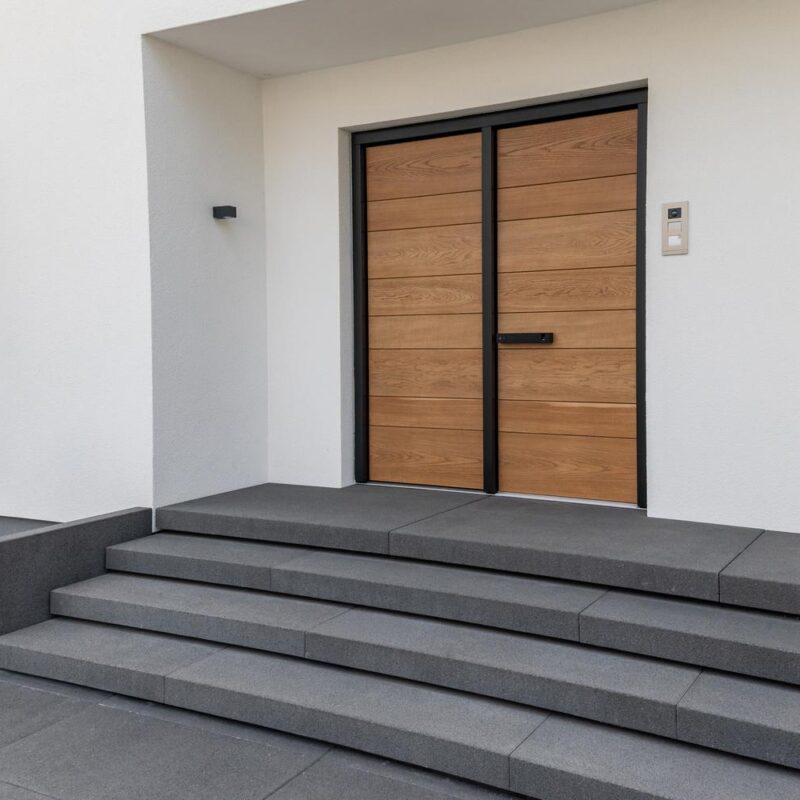 Breite Eingangstreppe aus dunklen Blockstufen vor moderner Holz-Haustür