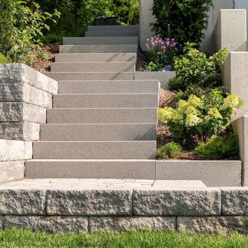 Gartentreppe mit Blockstufen zwischen Mauersteinen und bepflanzten Beeten