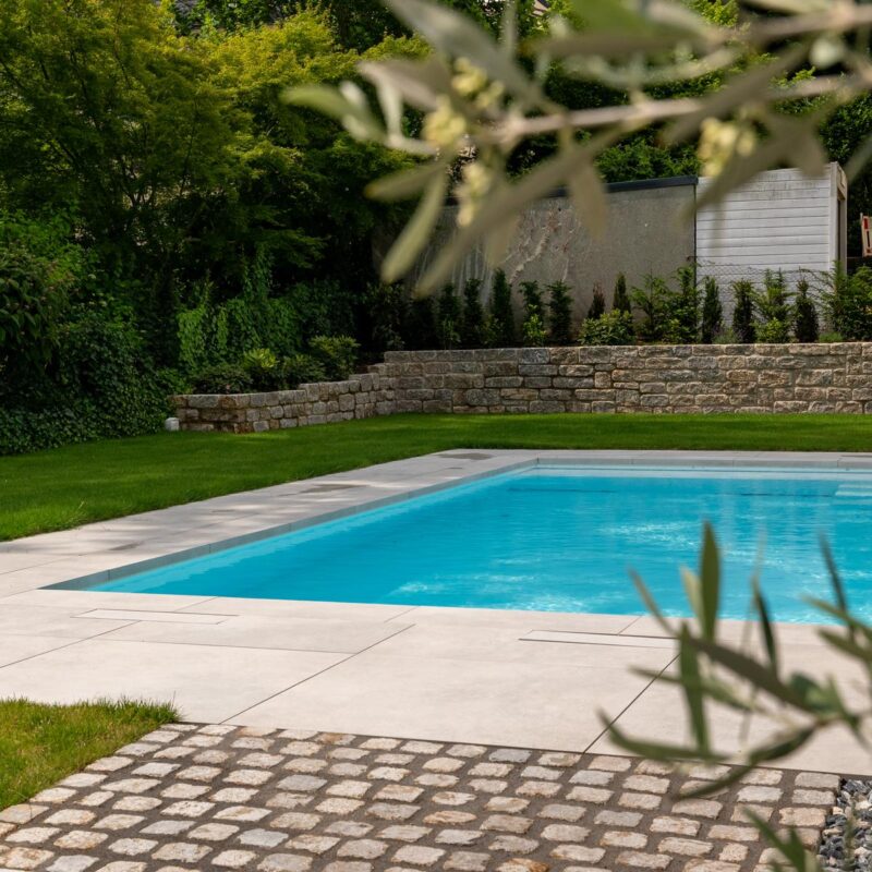 Pool mit Feinsteinzeug-Umrandung, Natursteinpflaster und Natursteinmauer