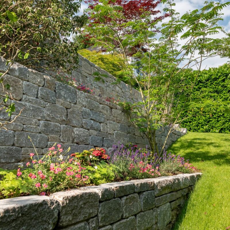 Trockenmauer aus Naturstein mit Staudenbeet und Rasen
